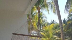 A hammock on a porch with a view of palm trees and a grassy area.