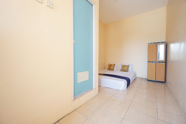 A small, single-room hotel room with a bed, a wardrobe, and a door.