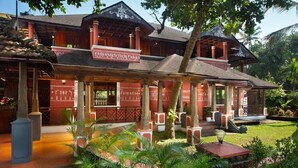 A traditional wooden building with a covered veranda, surrounded by lush greenery and palm trees. - Ananda Cherai (Kochi)