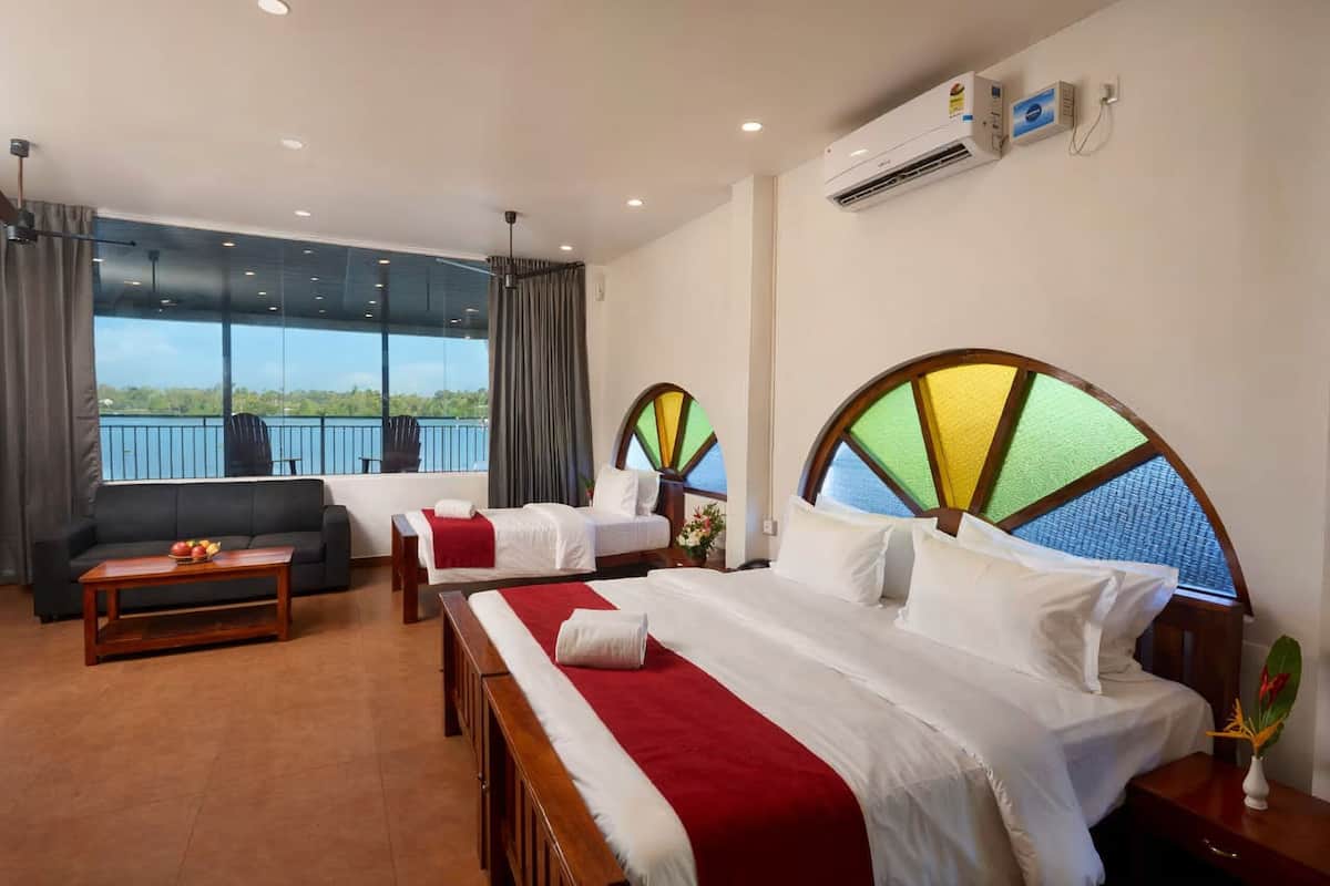 A hotel room with two beds, a sofa, a wooden table, and large windows with a view of the sea.