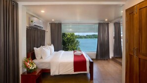 A hotel room with a large bed, a wooden wardrobe, and a view of a body of water. - Ananda Cherai (Kochi)