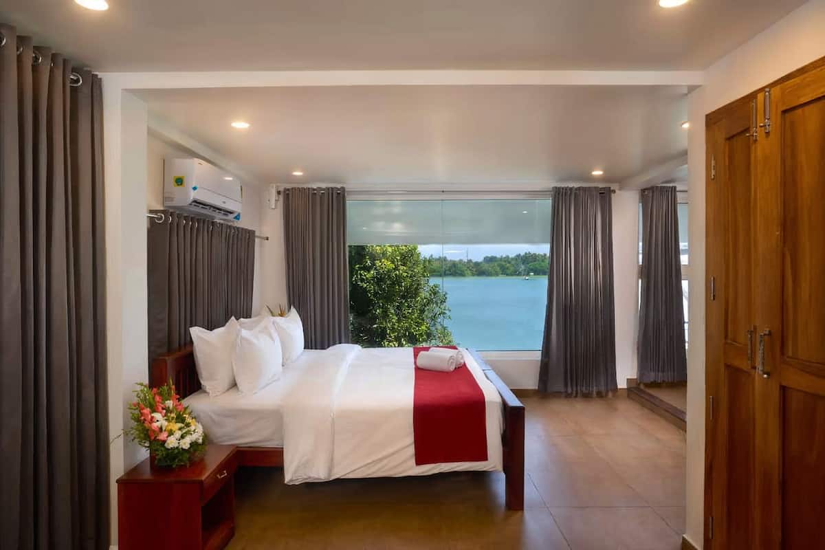 A hotel room with a large bed, a wooden wardrobe, and a view of a body of water.