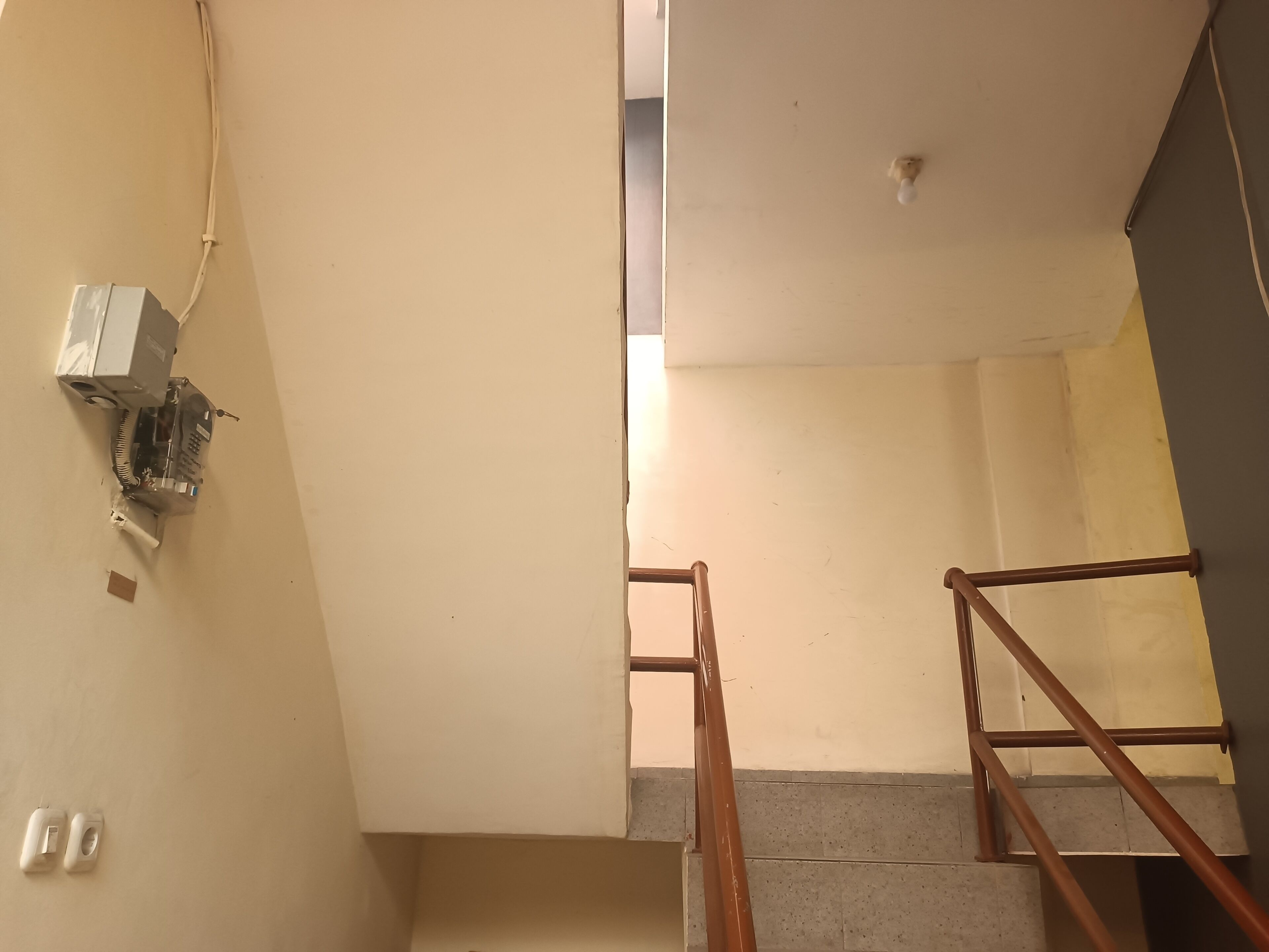 A staircase with a metal railing, a wall-mounted electrical box, and a door leading to another room.