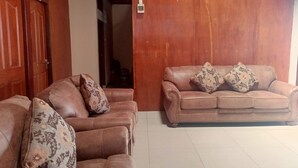A living room with two brown leather sofas, each with patterned cushions, and a wooden wall with a clock. - Hotel O Lourdes Blessing Hill (Manado)