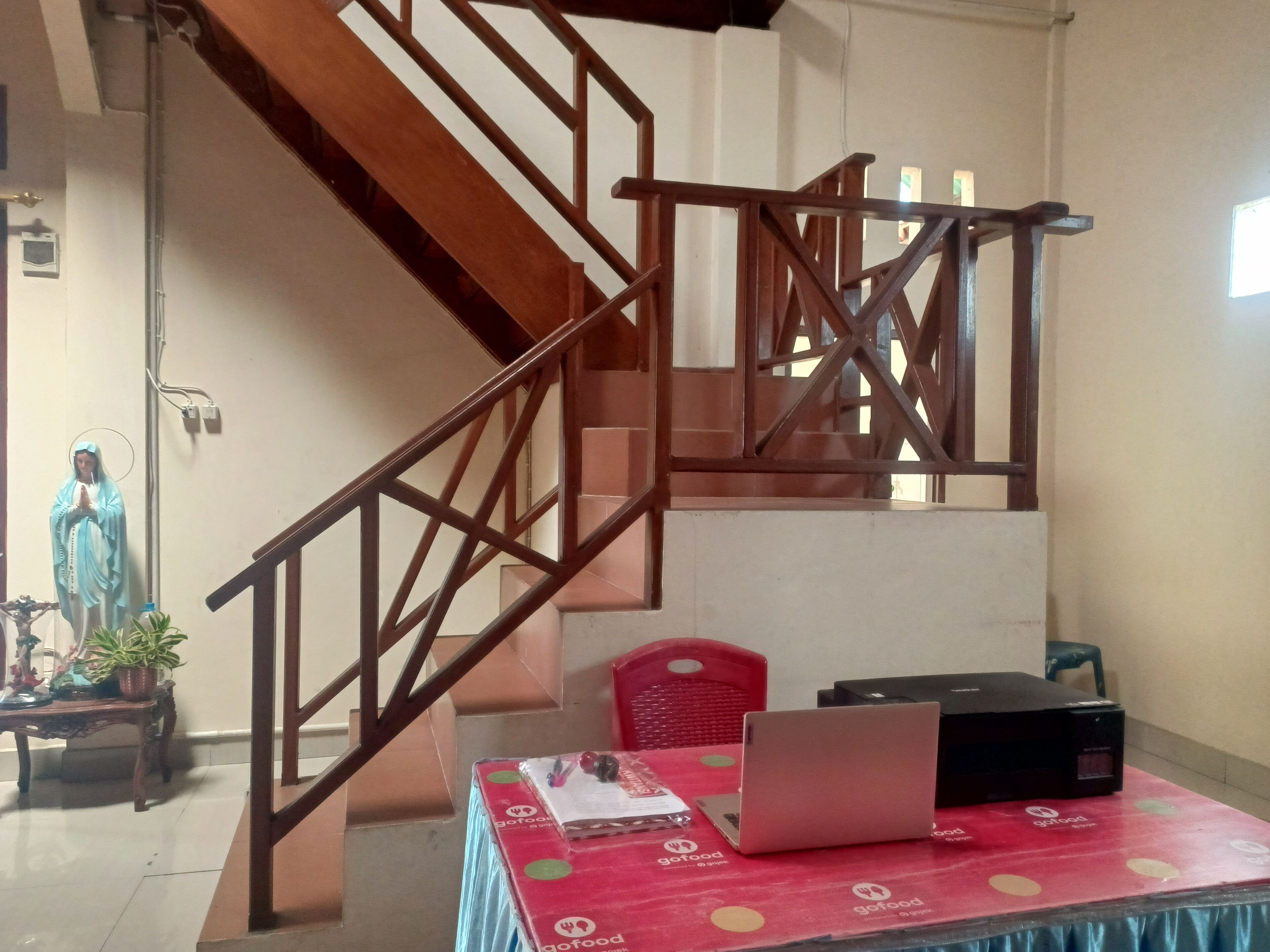 A staircase with wooden railings, a statue, a table with a laptop, and a red tablecloth with logos.