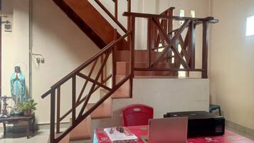 A staircase with wooden railings, a statue, a table with a laptop, and a red tablecloth with logos.