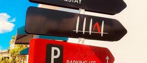 A directional sign with multiple arrows pointing in different directions, indicating various facilities such as a homestay and a parking lot.