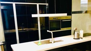 Una cucina moderna con un piano di lavoro bianco, elettrodomestici in acciaio inossidabile e sedie nere.
