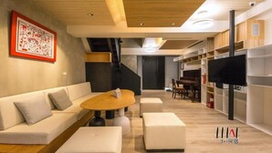 Un soggiorno moderno con un divano, poggiapiedi, un tavolino da caff è, una TV e scaffalature a muro.