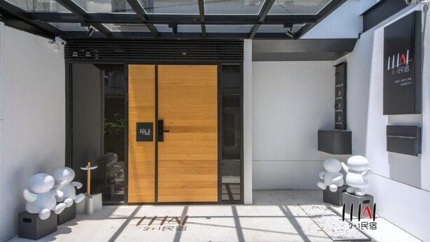 L'ingresso moderno di un hotel con una porta in legno, una tettoia in vetro e un logo sulla parete.