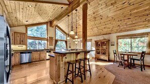 A spacious kitchen with wooden beams, a central island with stools, and a dining area with chairs. - Donner Adventure Lodge: Pet Friendly, Games, Bunks (Truckee)