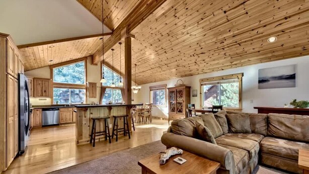 A spacious living area with a wooden ceiling, a leather sofa, and a kitchen in the background. - Donner Adventure Lodge: Pet Friendly, Games, Bunks (Truckee)