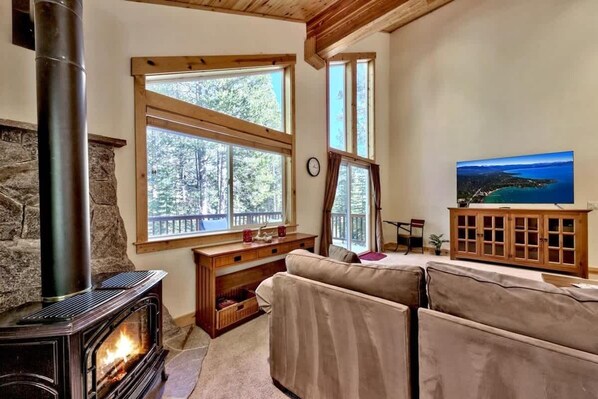 A cozy room with a stone fireplace, large windows, a sofa, and a television.