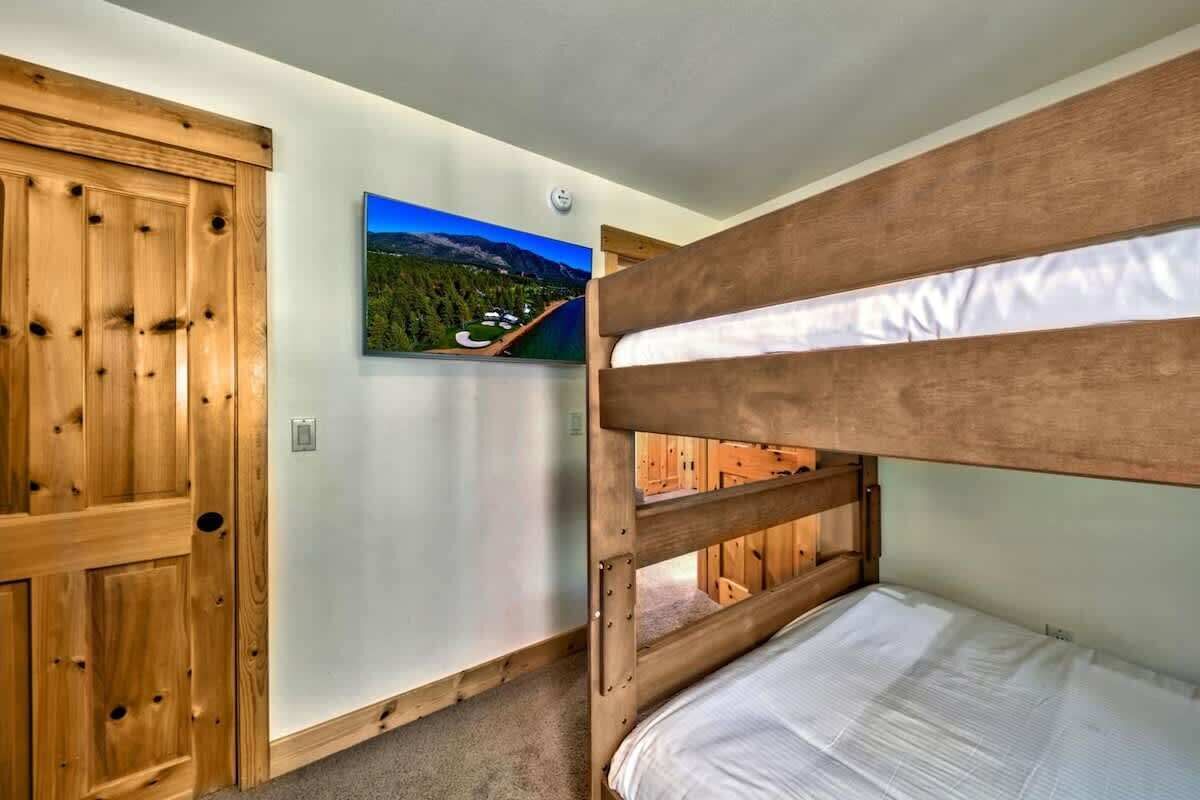 A bunk bed room with a wooden door and a framed landscape painting on the wall.