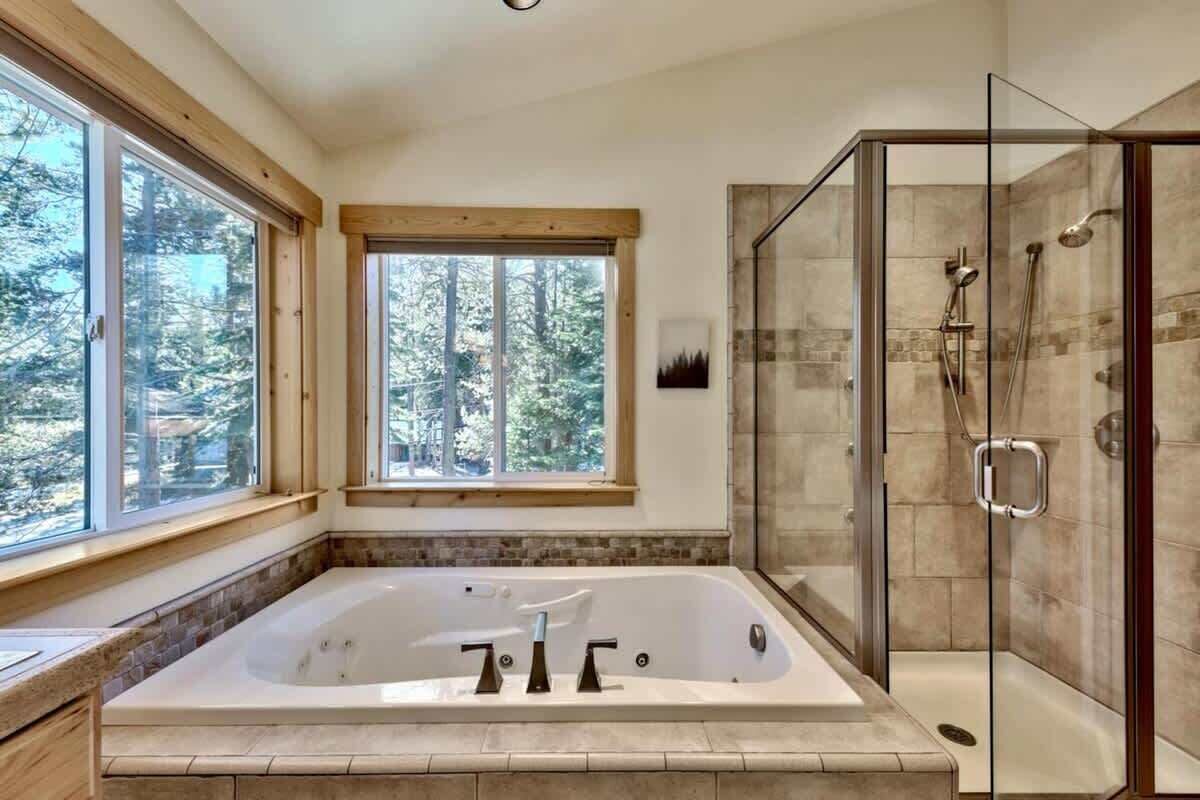 Ein Badezimmer mit einer großen Badewanne, einer Duschkabine aus Glas und einem Fenster mit Blick auf Bäume.