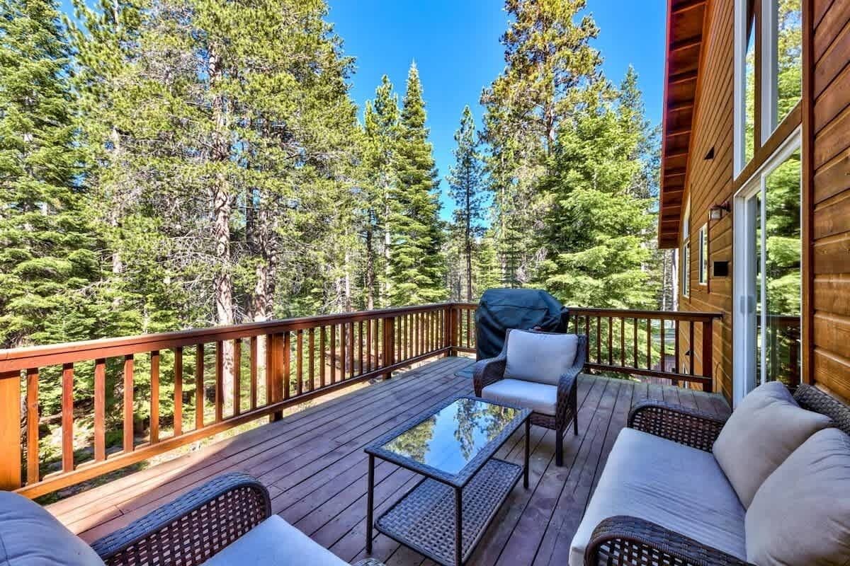 Une terrasse en bois, agrémentée de mobilier d’extérieur, entourée de grands arbres.