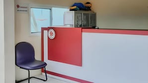 Un comptoir d’accueil aux couleurs rouge et blanche, une chaise bleue et une vitrine en verre.