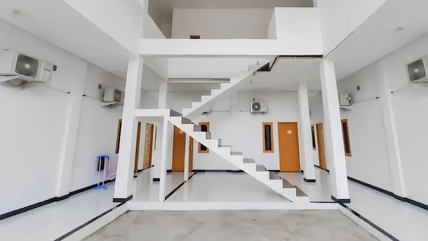 Un intérieur spacieux avec un escalier central, des murs blancs et de nombreuses portes.