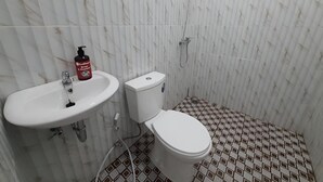 Une salle de bain avec un lavabo, des toilettes et une douche, le tout de couleur blanche. Les murs sont recouverts de carreaux imitant le marbre, et le sol présente un motif géométrique.