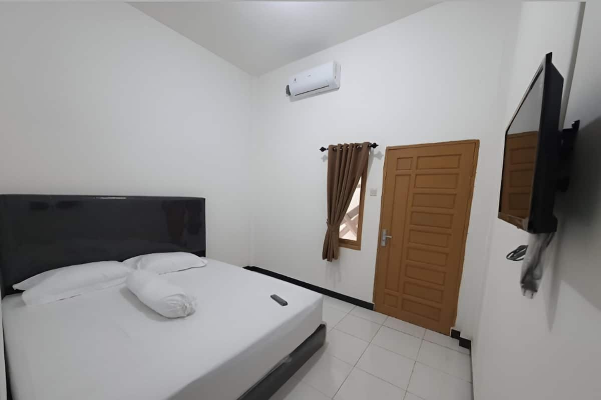 A bedroom with a bed, a TV mounted on the wall, a door, and an air conditioning unit.