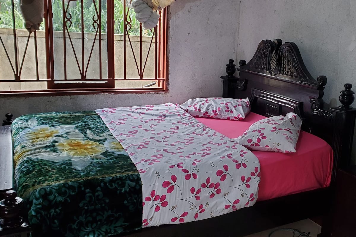 A bedroom with a bed, a window with bars, a mirror, and a wardrobe.