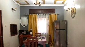A compact kitchen with a refrigerator, a dining table with chairs, a microwave, and a small cabinet. - Dream Day Cottages (Kampala)