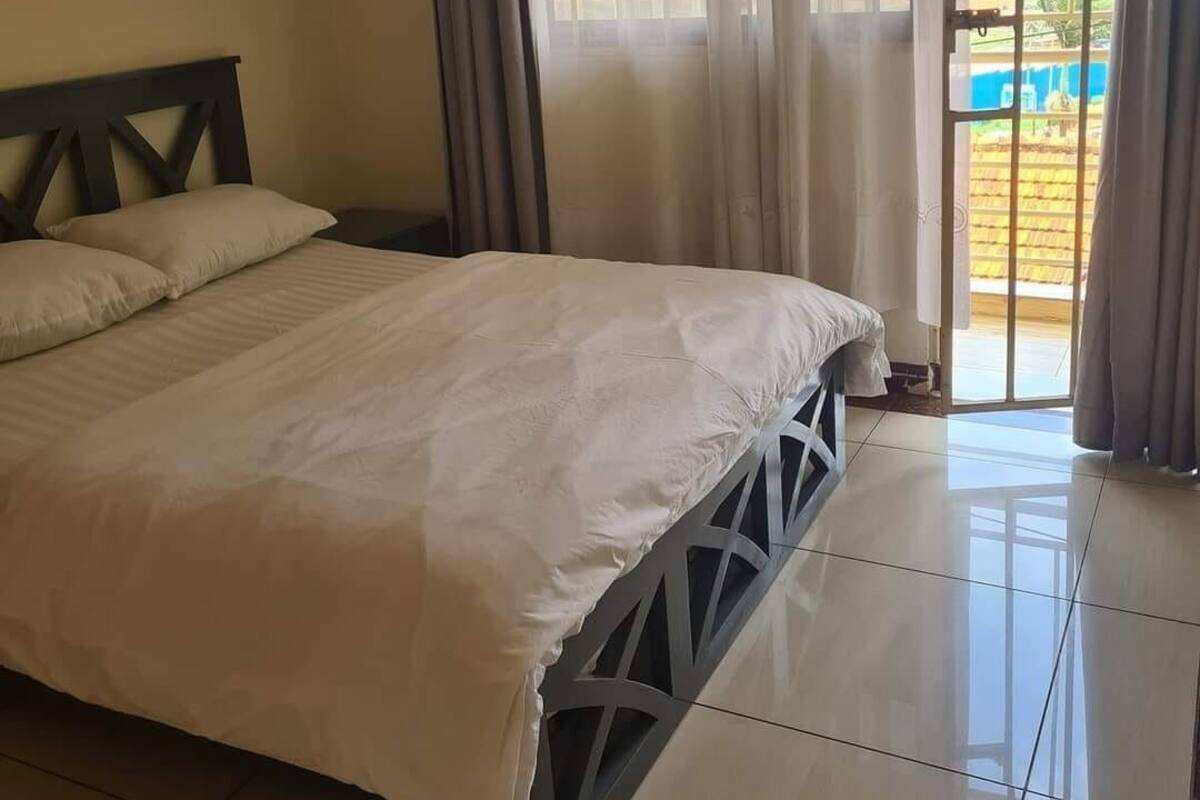 A bedroom with a bed, curtains, and a view of a garden through a window.