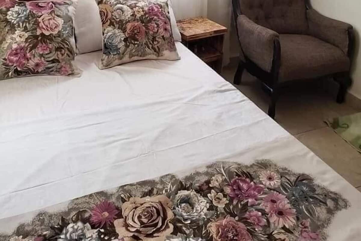 A bedroom with a wooden headboard, floral bedding, a brown armchair, and a small wooden nightstand.