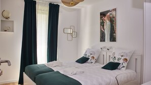 Un dormitorio ordenado con cama, mesita de noche, lámpara de pared y ventana con cortinas.
