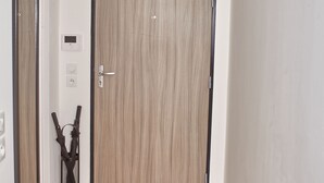 Un pasillo con piso de madera, una puerta con cerradura digital y una lámpara en el techo.