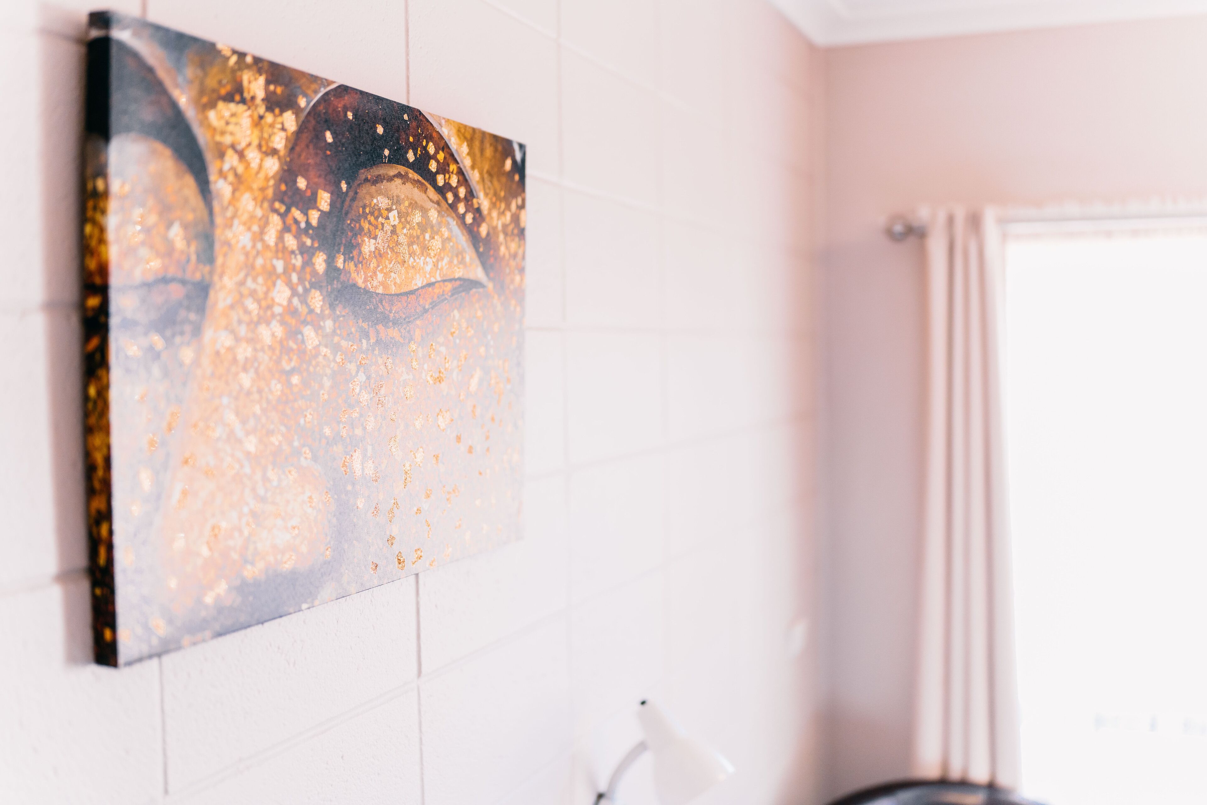 Un baño con pared de azulejos blancos, un cuadro y una ventana con cortinas.
