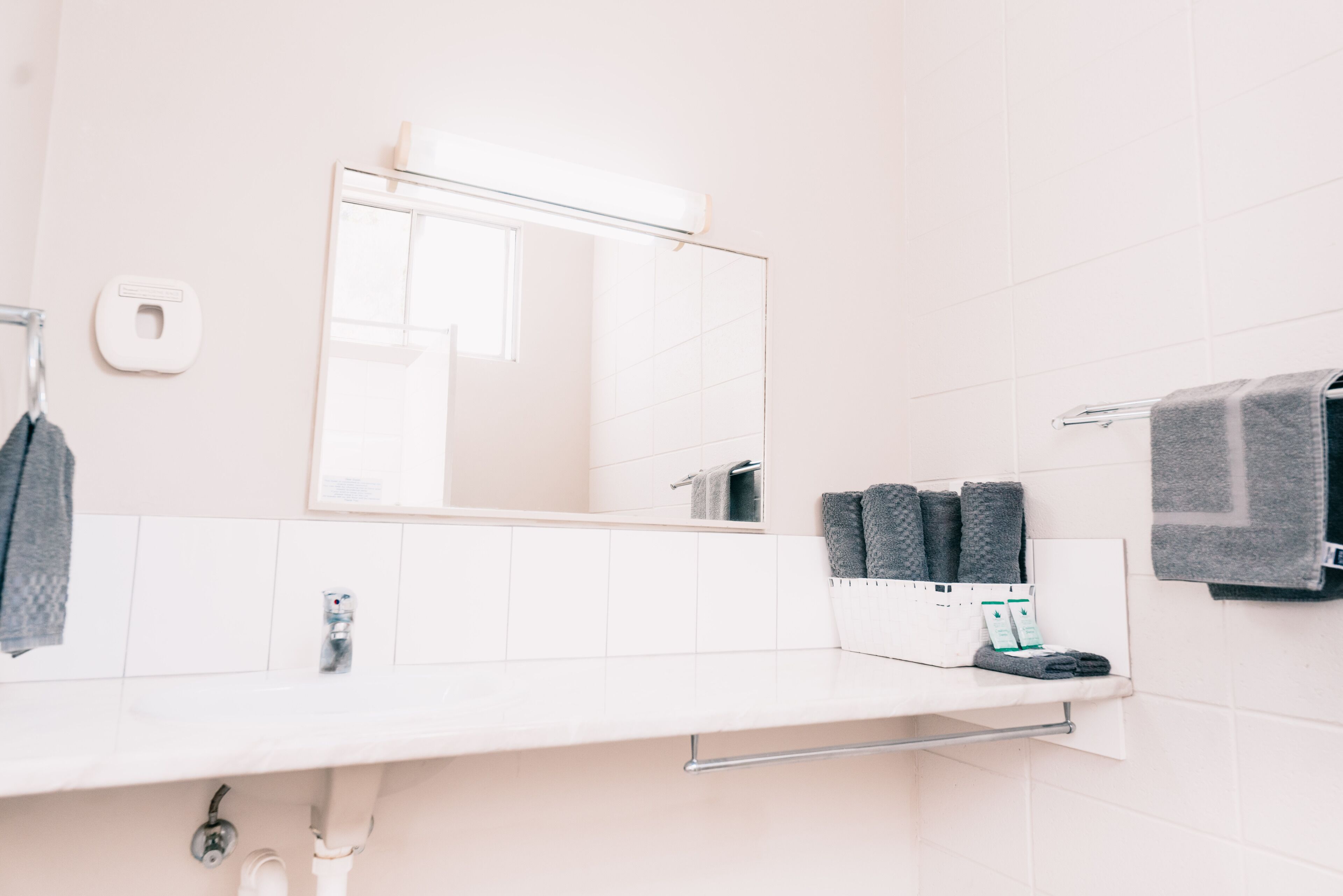 Ein Badezimmer mit weißem Waschbecken, Spiegel, Handtuchhalter und Seifenspender.