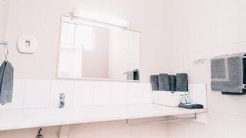 Ein Badezimmer mit weißem Waschbecken, Spiegel, Handtuchhalter und Seifenspender.