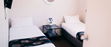 Una habitación de hotel con dos camas individuales, una mesita con un jarrón de flores y un espejo en la pared.