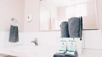 Un baño con un lavamanos blanco, un espejo y dos toallas enrolladas sobre el mostrador.