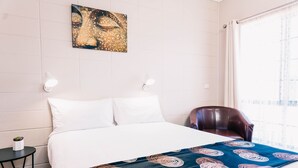 A hotel room with a bed, a chair, a small table with a plant, and a painting on the wall. - Motel Poinsettia (Port Augusta West)