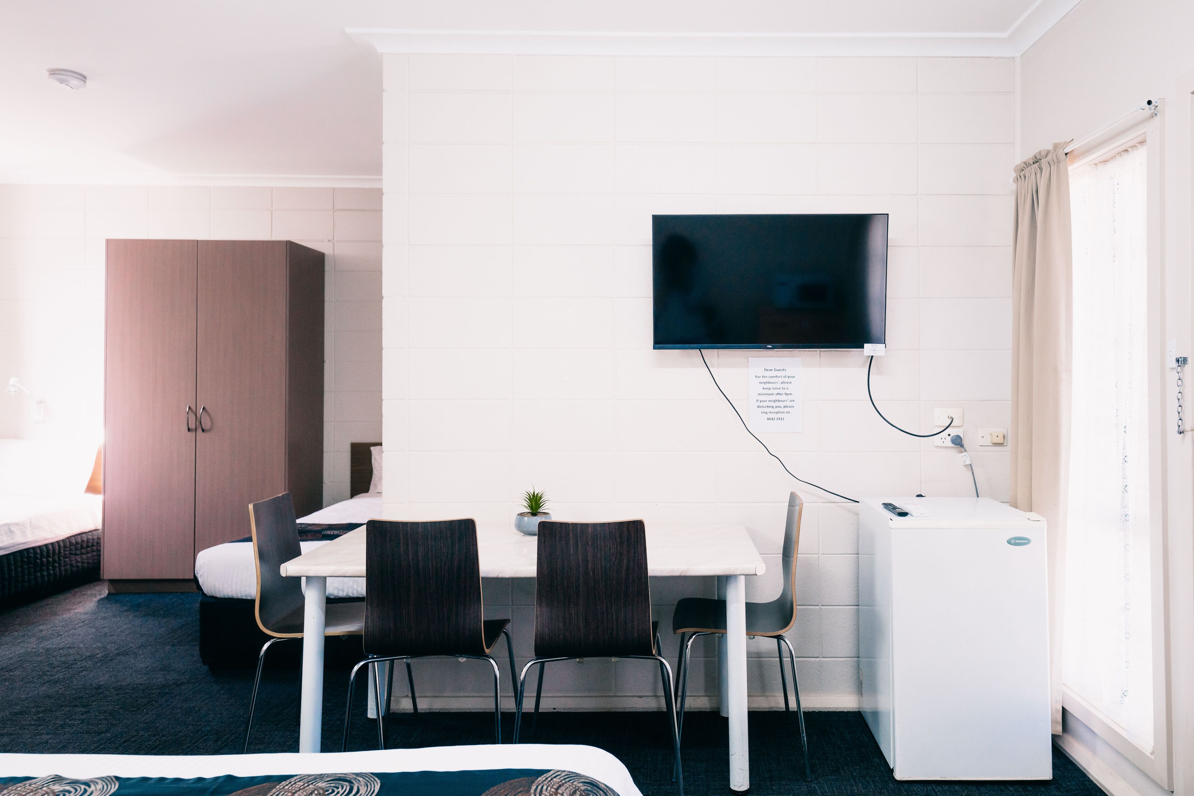 Ein Hotelzimmer mit einem Bett, einem Schreibtisch mit zwei Stühlen, einem Fernseher und einem Kleiderschrank.