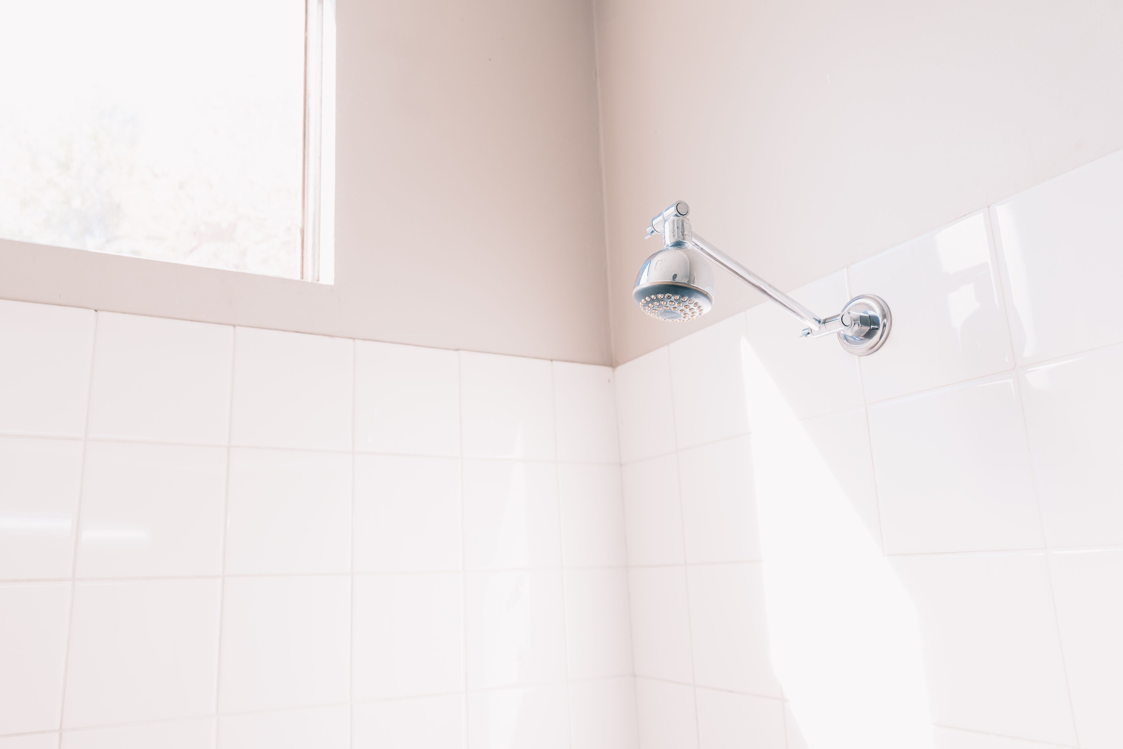 A showerhead mounted on a white tiled wall in a bathroom.