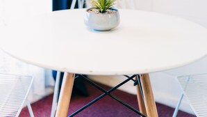 A round white table with a small potted plant, a white chair, and a colorful abstract painting on the wall. - Motel Poinsettia (Port Augusta West)