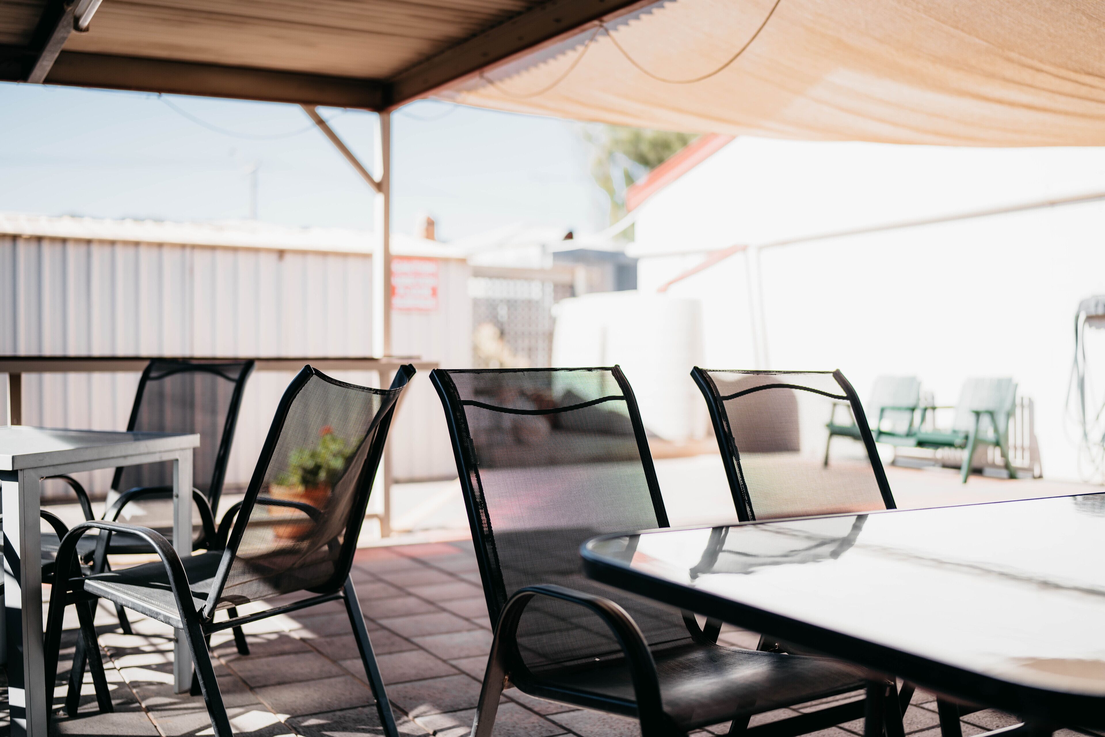 An outdoor patio area with metal chairs and a table, under a shaded canopy.