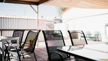 An outdoor patio area with metal chairs and a table, under a shaded canopy.