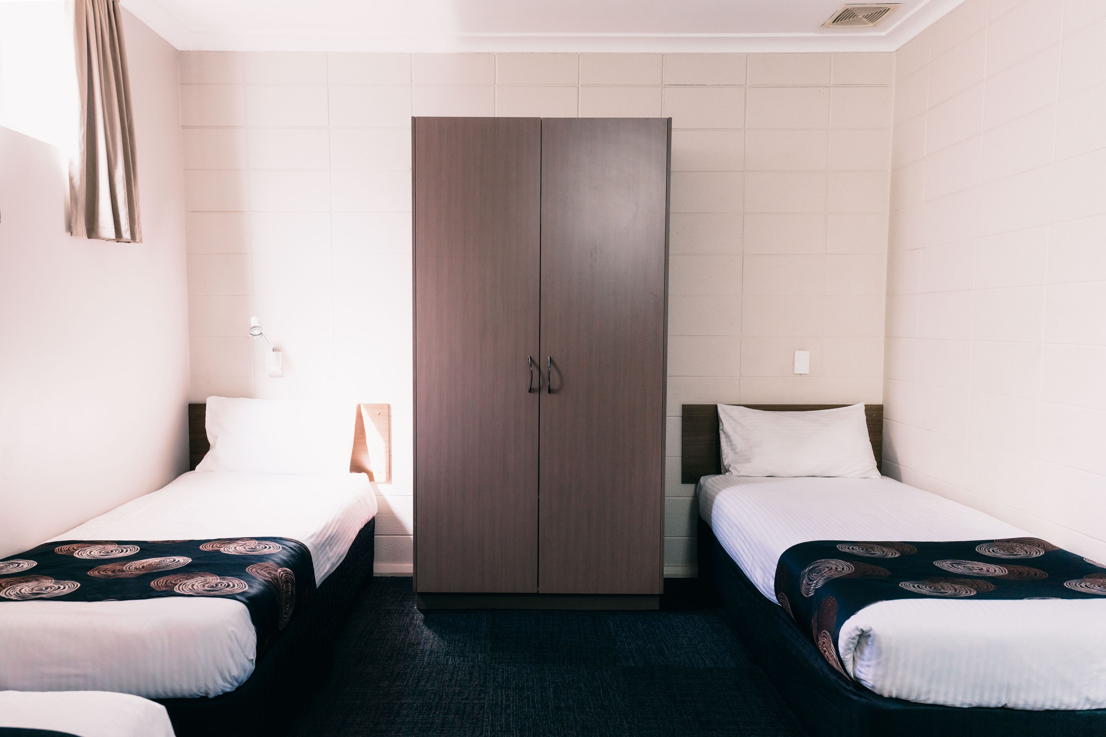 A hotel room with two single beds, a wardrobe, and a small bedside table.