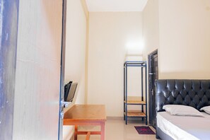 A bedroom with a bed, a wooden table, a metal shelf, and a door. - Hotel O Rinjani Guest House (Balikpapan)