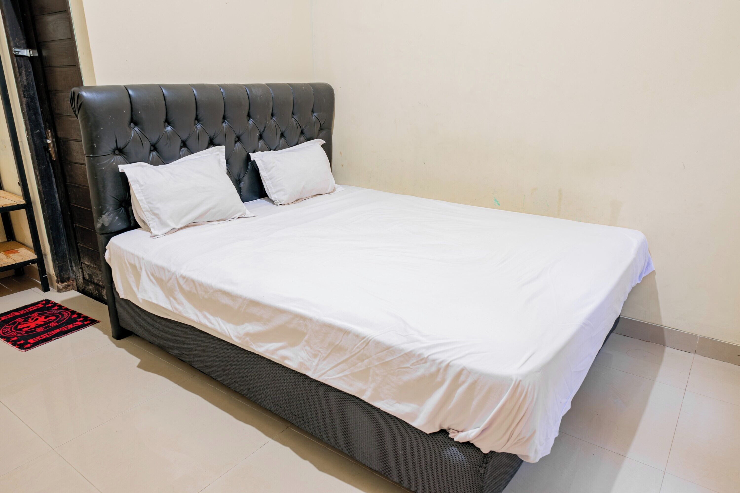 A bed with a tufted headboard, white bedding, and a red and black patterned rug.
