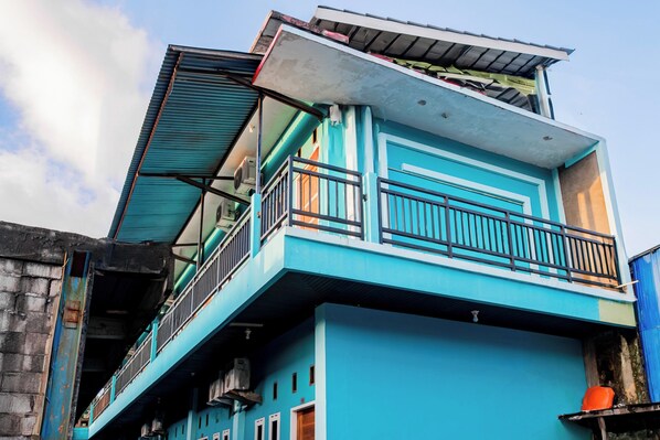A multi-story building with a blue exterior, a balcony on the upper floor, and a visible door on the ground floor.