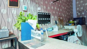 A reception desk with a sign, a plant, a computer, and a fan. - Hotel O Rinjani Guest House (Balikpapan)
