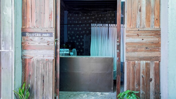 A reception area with a wooden door, a reception desk, and a sign indicating the reception room. - Hotel O Rinjani Guest House (Balikpapan)
