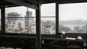 Una habitación con un ventanal grande con vistas a la ciudad, una mesa de mármol con una taza y un florero, y varias sillas.