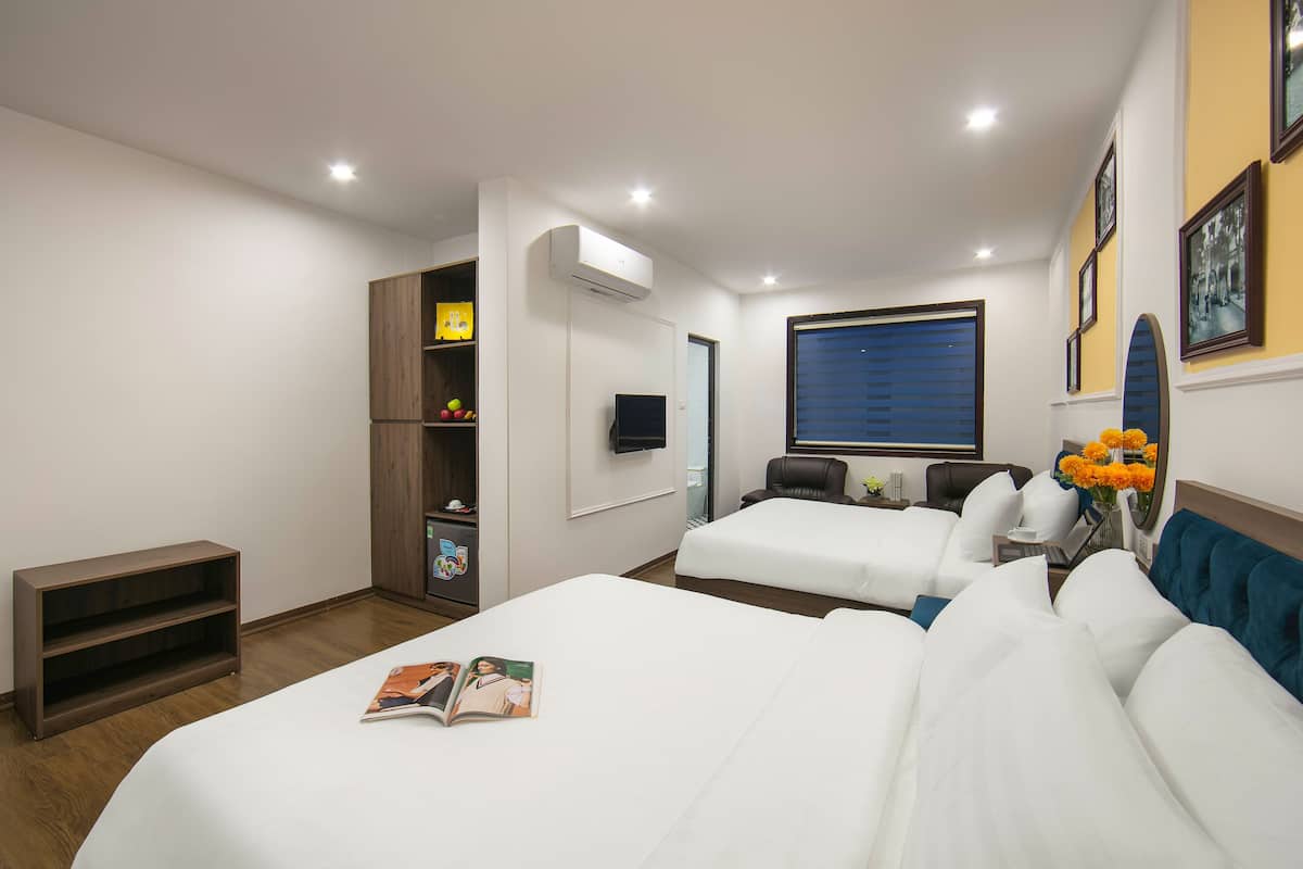 A hotel room with two beds, a TV, a bookshelf, and a window with blinds.