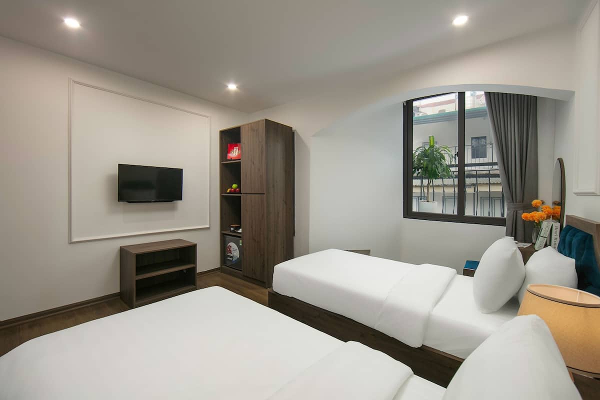 A hotel room with two beds, a TV, a wardrobe, and a window with a view of the outside.